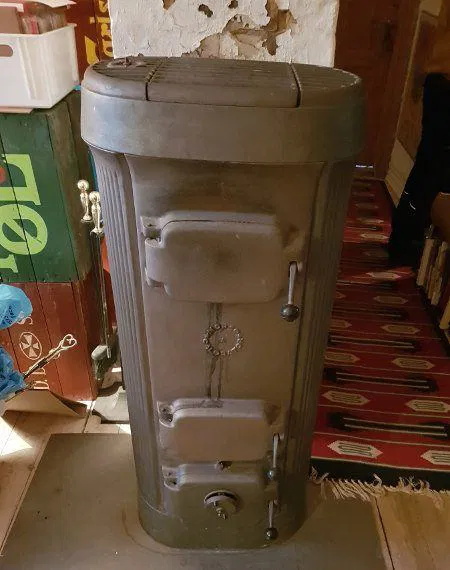 Billede af vintage cylindrisk støbejernsovn i støbejern med tre låger, håndtag og dekorativt mønster, egnet som træ- eller kulovn