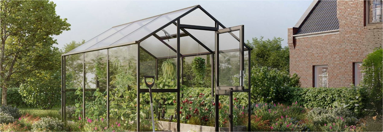 Glasdrivhus med sort aluminiumsramme, åben dør, planter og en skovl i en frodig have foran et murstenshus
